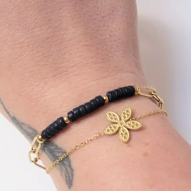 Bracelet femme doré et noir en acier inoxydable avec fleur élégante porté au poignet
