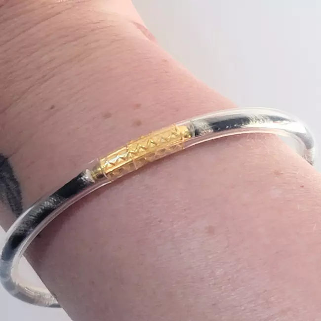 Bracelet jonc femme argenté en acier inoxydable avec détail doré porté au poignet