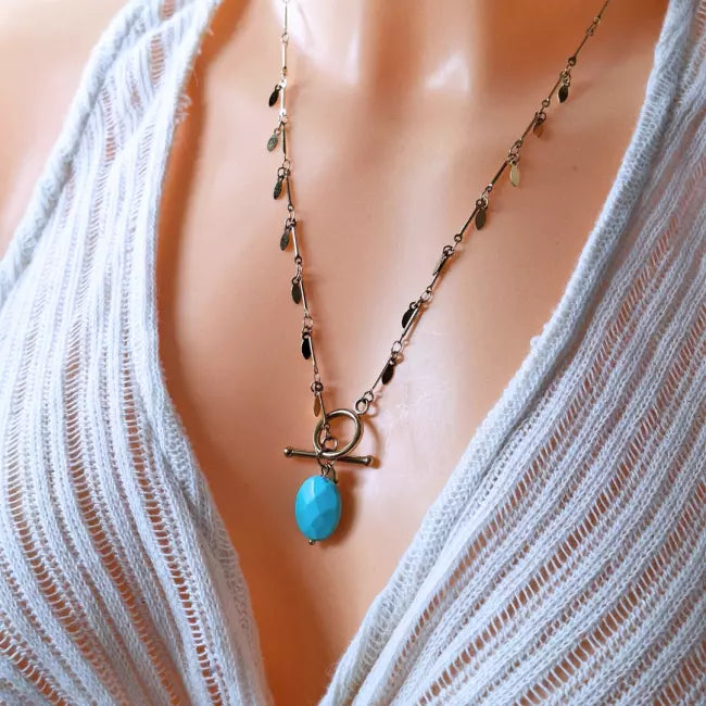 Collier doré femme en acier inoxydable porté, pendentif bleu effet pierre ovale, chaîne pampilles avec fermoir toggle.