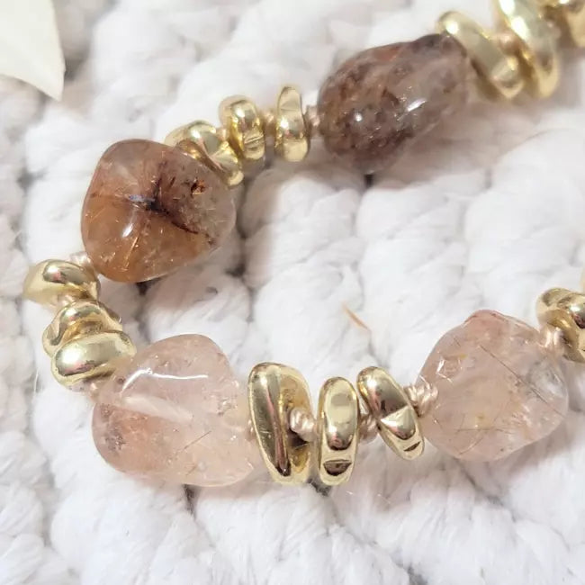 Gros plan sur collier doré avec perles irrégulières et pierres naturelles translucides brun-rosé, séparateurs dorés.