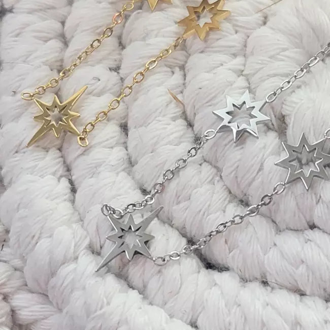 Colliers étoile du nord en acier inoxydable doré et argenté, pendentifs ajourés sur chaîne fine, posés sur fond tissé.