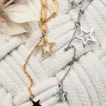 Collier étoile en acier inoxydable doré et argenté, chaîne à gros maillons avec pendentifs étoiles, présenté sur fond tissé.