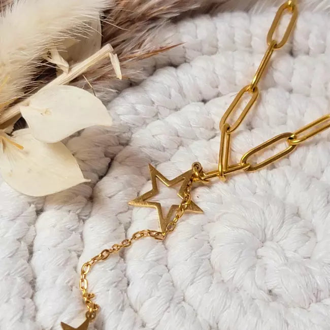 Collier étoile doré en acier inoxydable, chaîne à gros maillons avec pendentif étoile ajourée et étoile pleine, sur fond tissé.