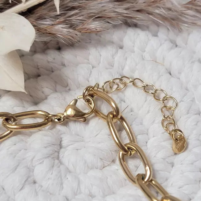 Détail du fermoir mousqueton et chaînette d’extension du collier fleur doré, gros plan.