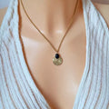 Collier pendentif doré porté – chaîne fine et médaillon rond texturé avec cabochon bleu pailleté, aperçu de la longueur sur le décolleté.