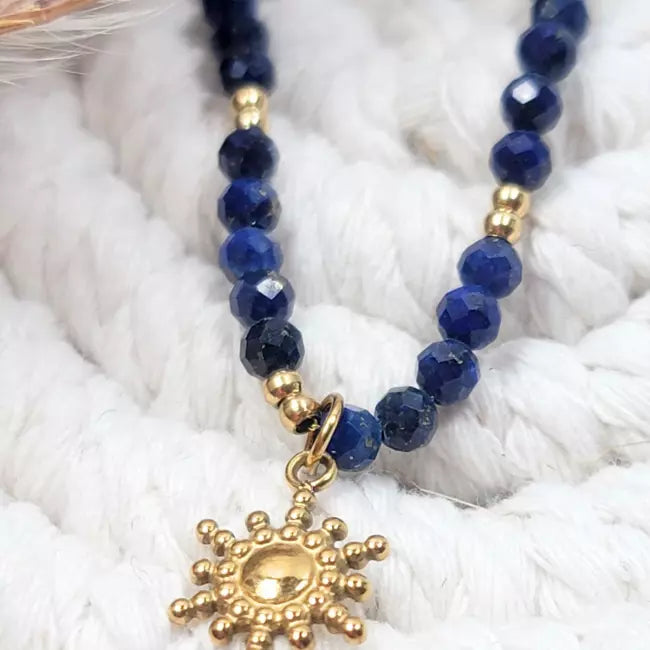 Gros plan sur pendentif soleil doré et perles facettées bleu marine du collier femme.